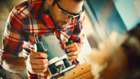 A man sanding down a piece of wood with an electric sander.