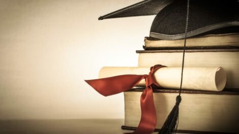 A stack of books with a graduation cap setting on top.