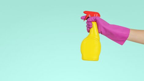 Person wearing gloves holding cleaning spray bottle.